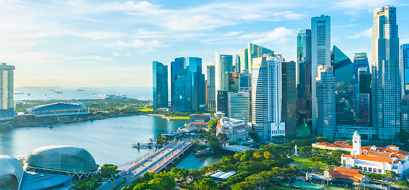 A skyline of Singapore with various buildings and the sun setting in the background.